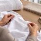 A buyer inspects the hem of a white linen sample beside a folded towel, table-linen sample and empty packing sleeve.