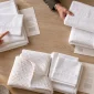 Hands compare separate groups of white sheet and towel samples beside allocation sheets on a planning table.