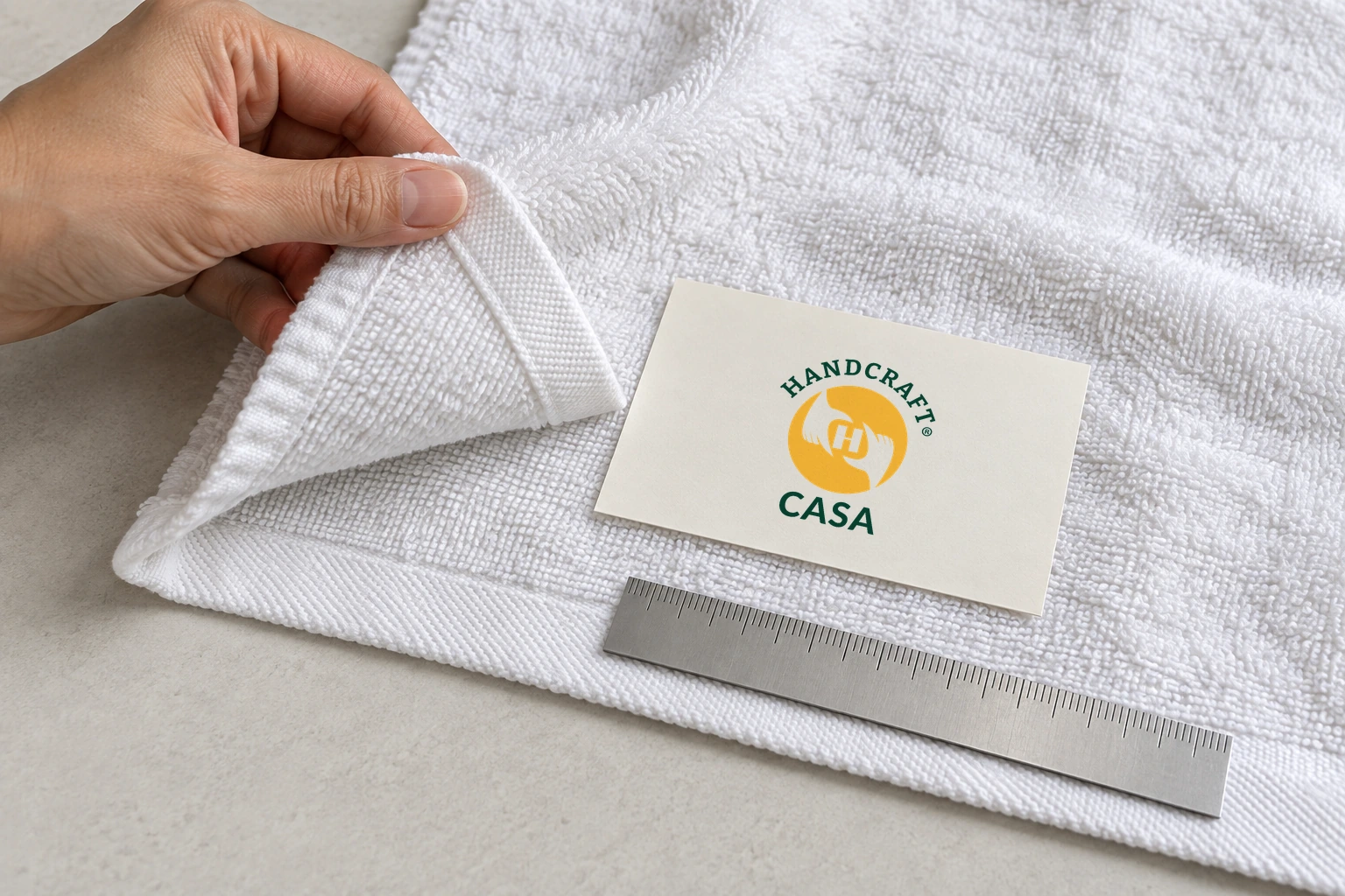 A hand inspects a white towel edge beside a Casa artwork-reference card and ruler.