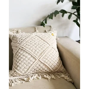 Cream cushion cover with raised diamond patterns and fringe on a beige armchair.