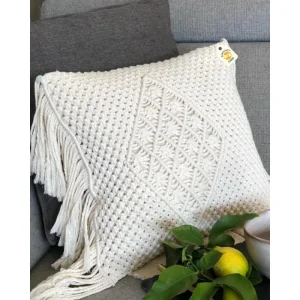 Cream cushion cover with a raised central diamond pattern and long side fringe on a grey sofa.