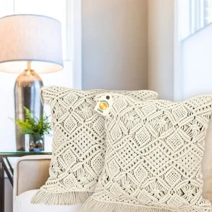 Two cream cushion covers with raised diamond patterns and fringe on a beige sofa.