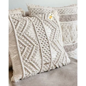 Cream cushion covers with raised geometric patterns and fringe on a neutral seat.