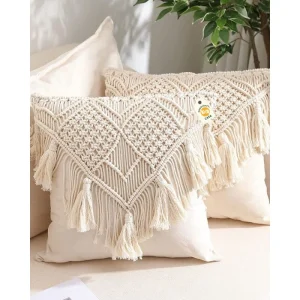 Two cream cushion covers with raised diamond patterns, layered fringe and tassels on a neutral sofa.