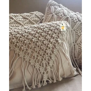 Three cream cushions with raised knotted patterns and long fringe arranged together on seating.