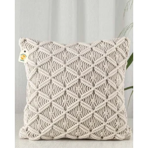 Cream cushion with an open diamond pattern against a pale wall, with green leaves at the side.