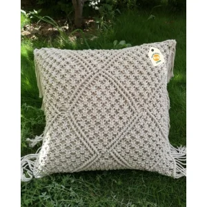 Cream cushion with dense raised geometric patterns and side fringe resting on grass.