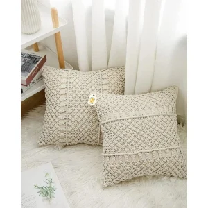 Two cream cushions with open geometric patterns on a white rug beside a shelf and curtains.