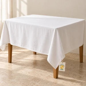 White plain cotton tablecloth draped over a dining table with a removable Casa tag.