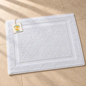 White terry bath mat laid flat on a stone floor with a removable Casa paper tag.