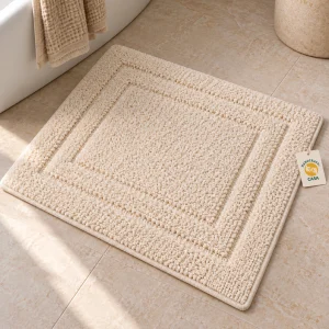 Cream tufted cotton bath mat laid flat beside a bathtub with a removable Casa presentation tag.